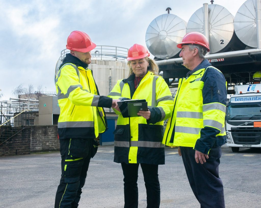 Three employees in High Viz looking at the arrival schedule for Tennants Bitumen