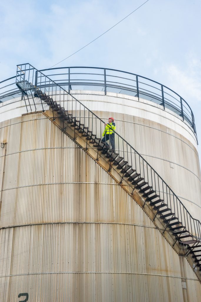 Employee at Tennants Bitumen climbing the curved stairs on the outside of a large tank
